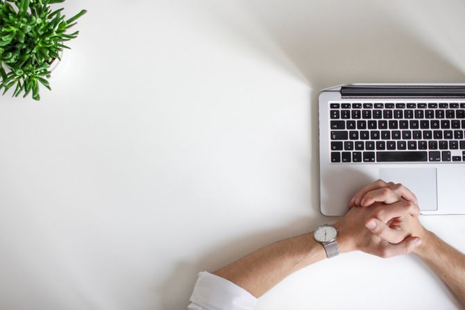 A person is sitting at a desk with their hands folded in front of a laptop computer.