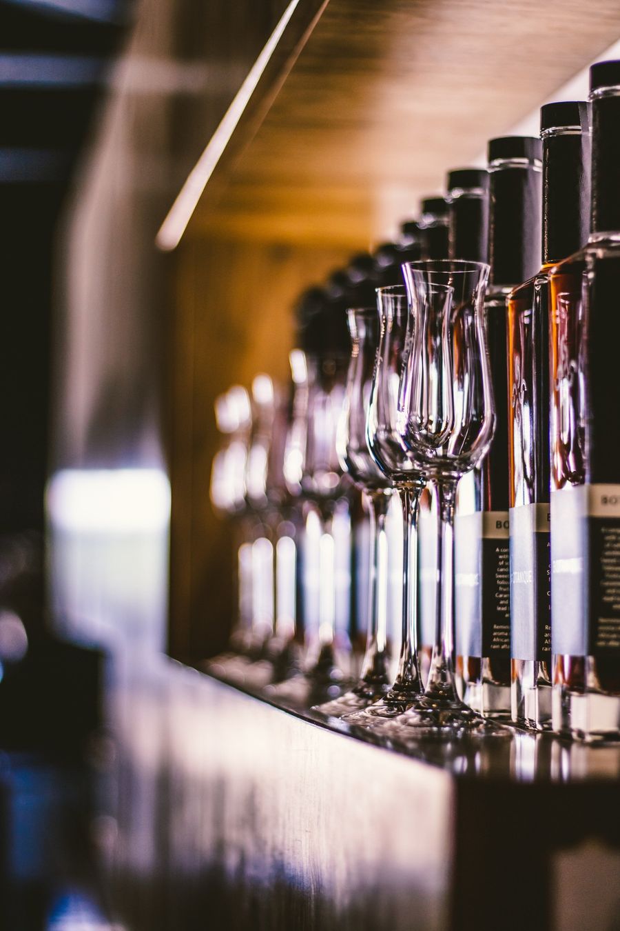 A row of wine glasses and bottles on a shelf.