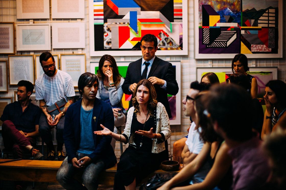 A group of people are sitting in a room with paintings on the wall.