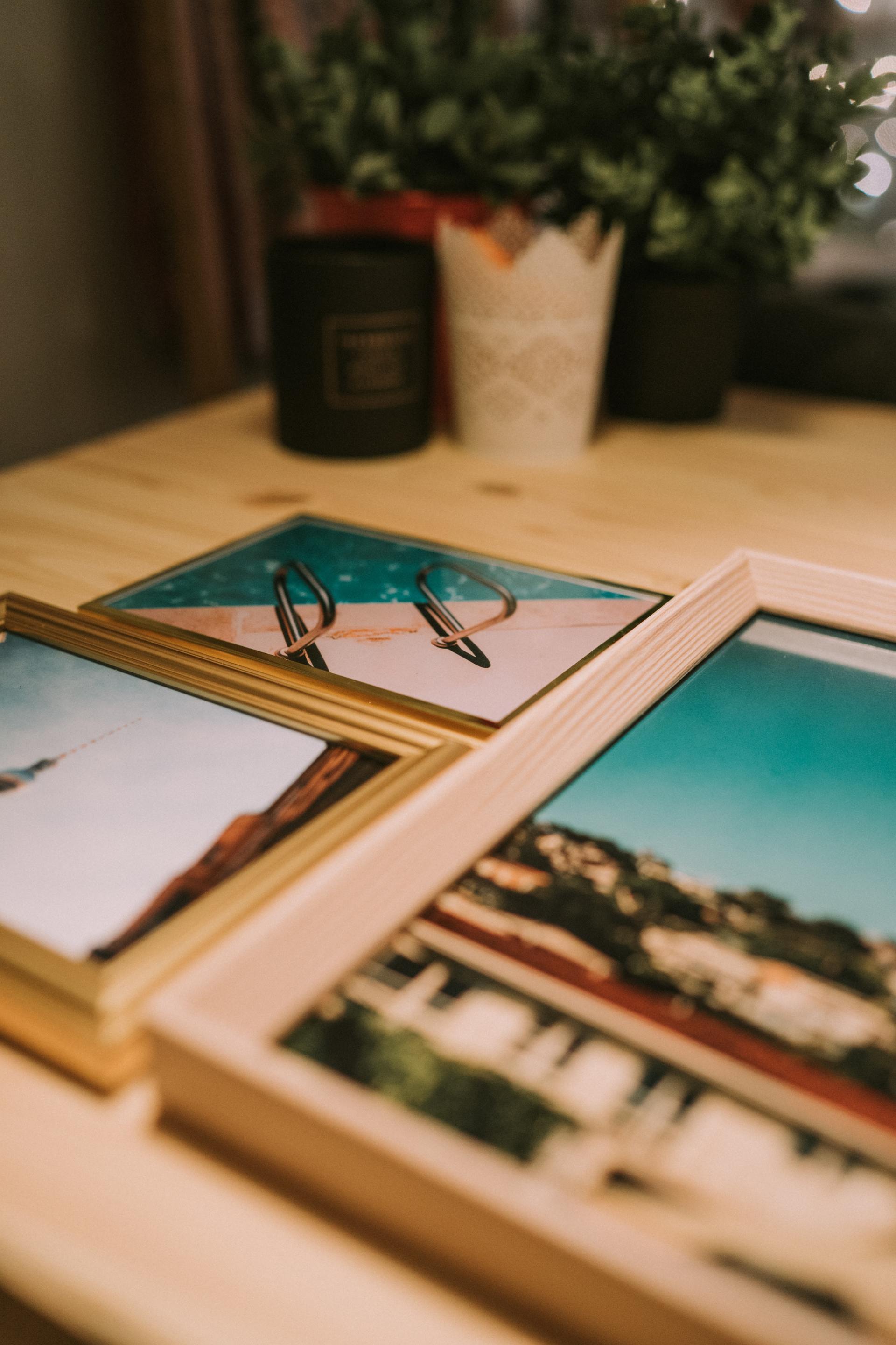 Framed travel photos on a wooden surface with plants and candle in the background.