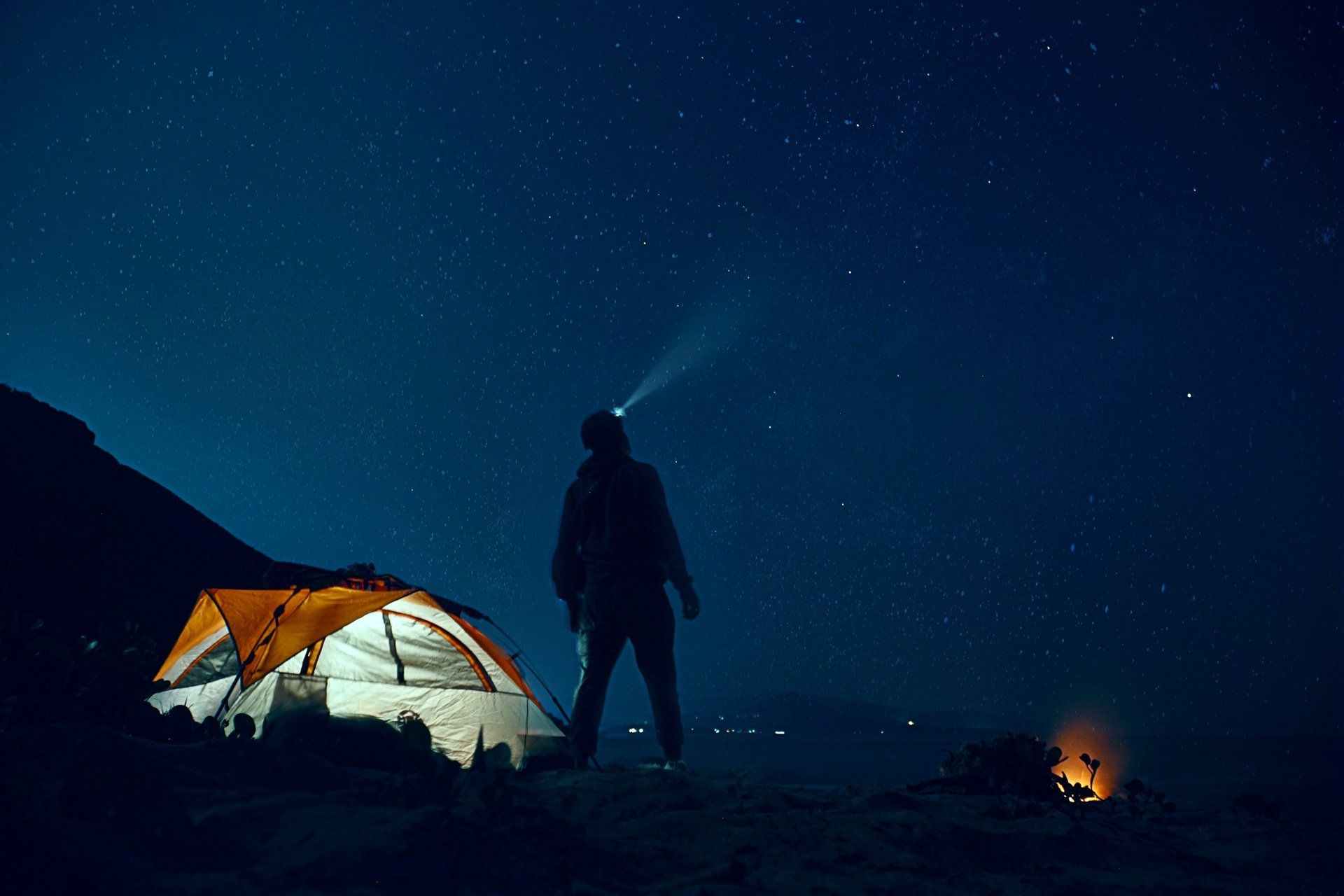 A man is standing in front of a tent at night.