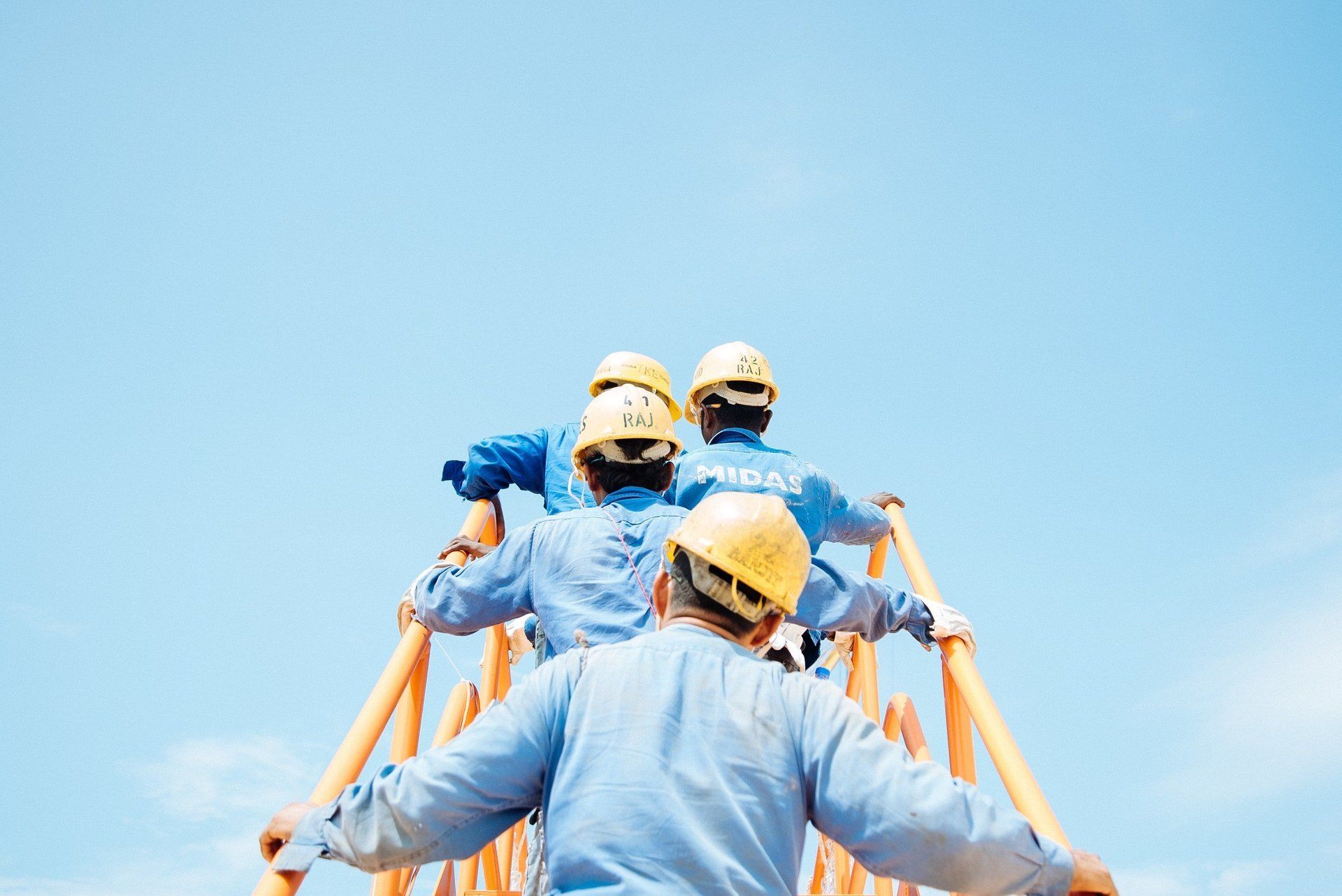 rear view of four workmen in yellow helmets climbing stairs