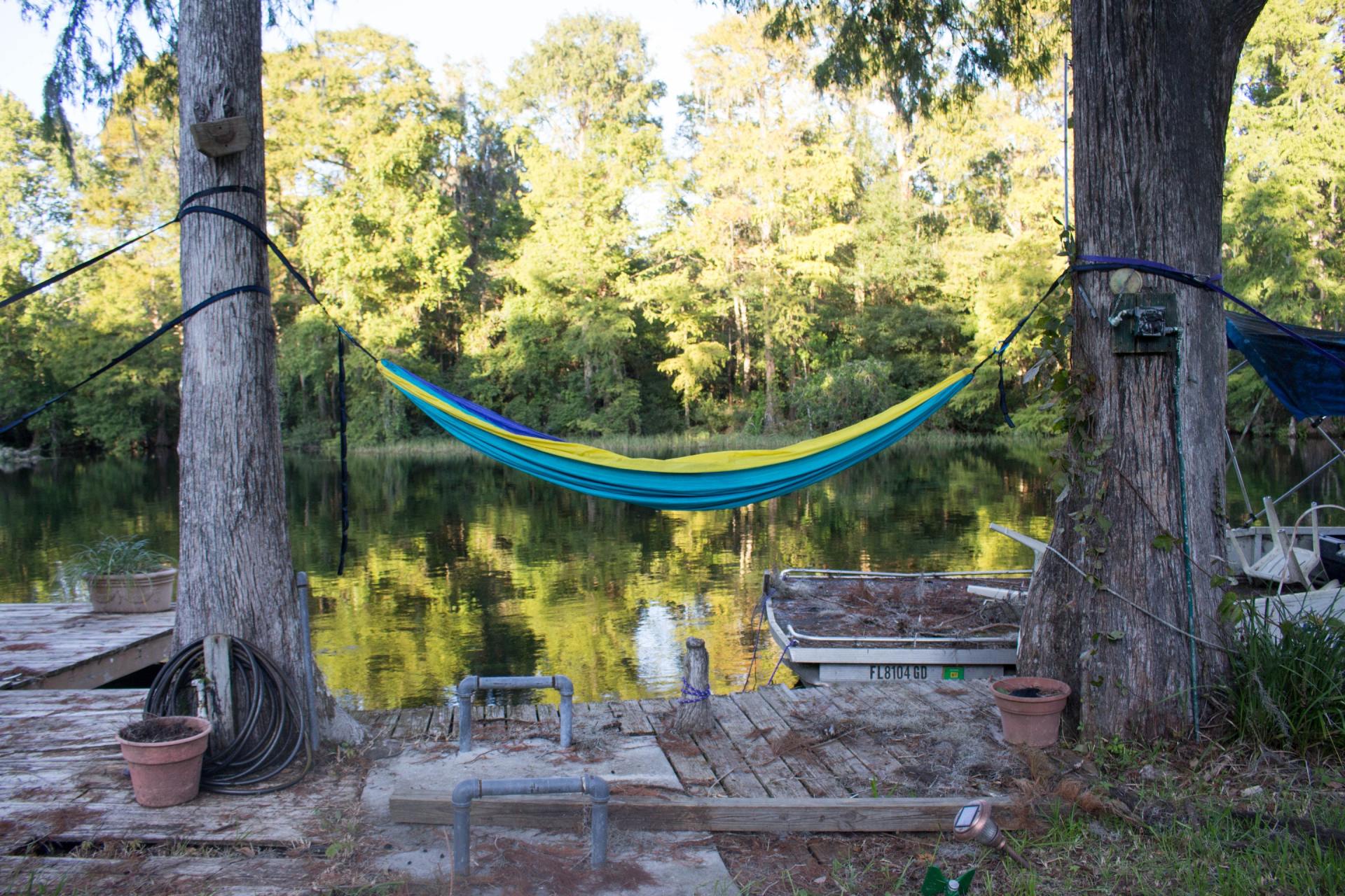 A blue and yellow hammock is hanging between two trees next to a lake.