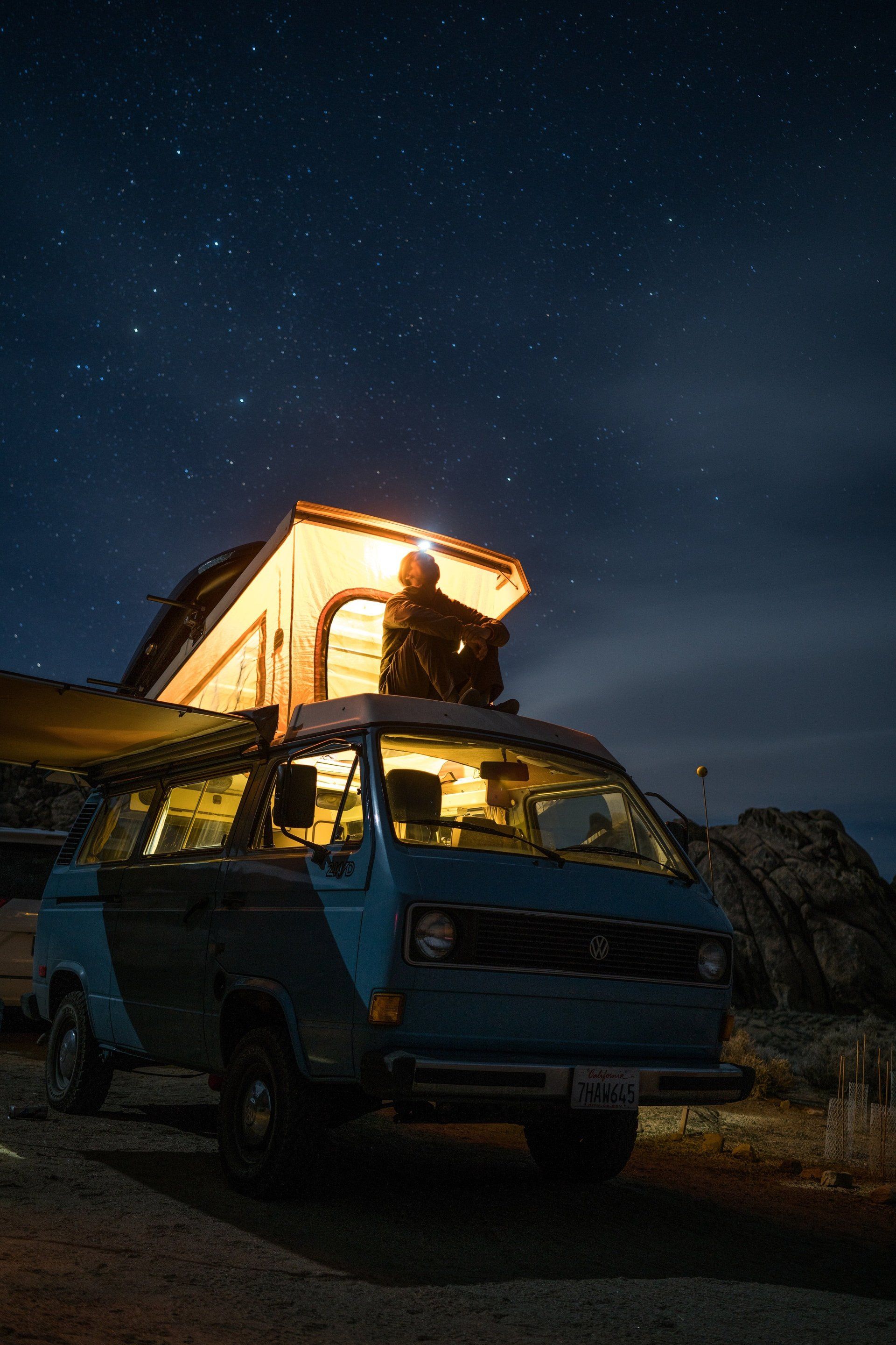 A man is sitting on top of a camper van at night.