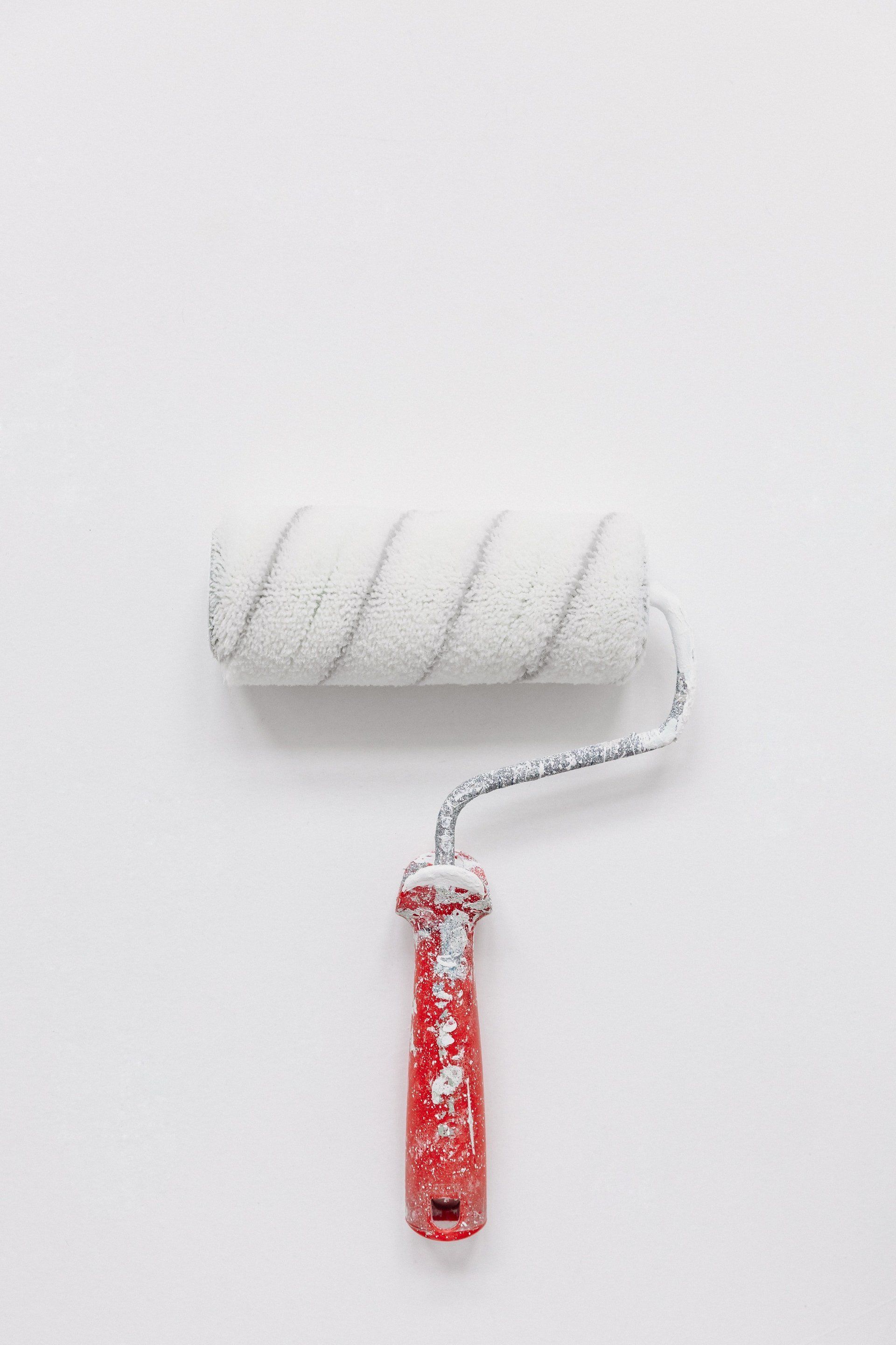 small paint roller with white paint and red handle
