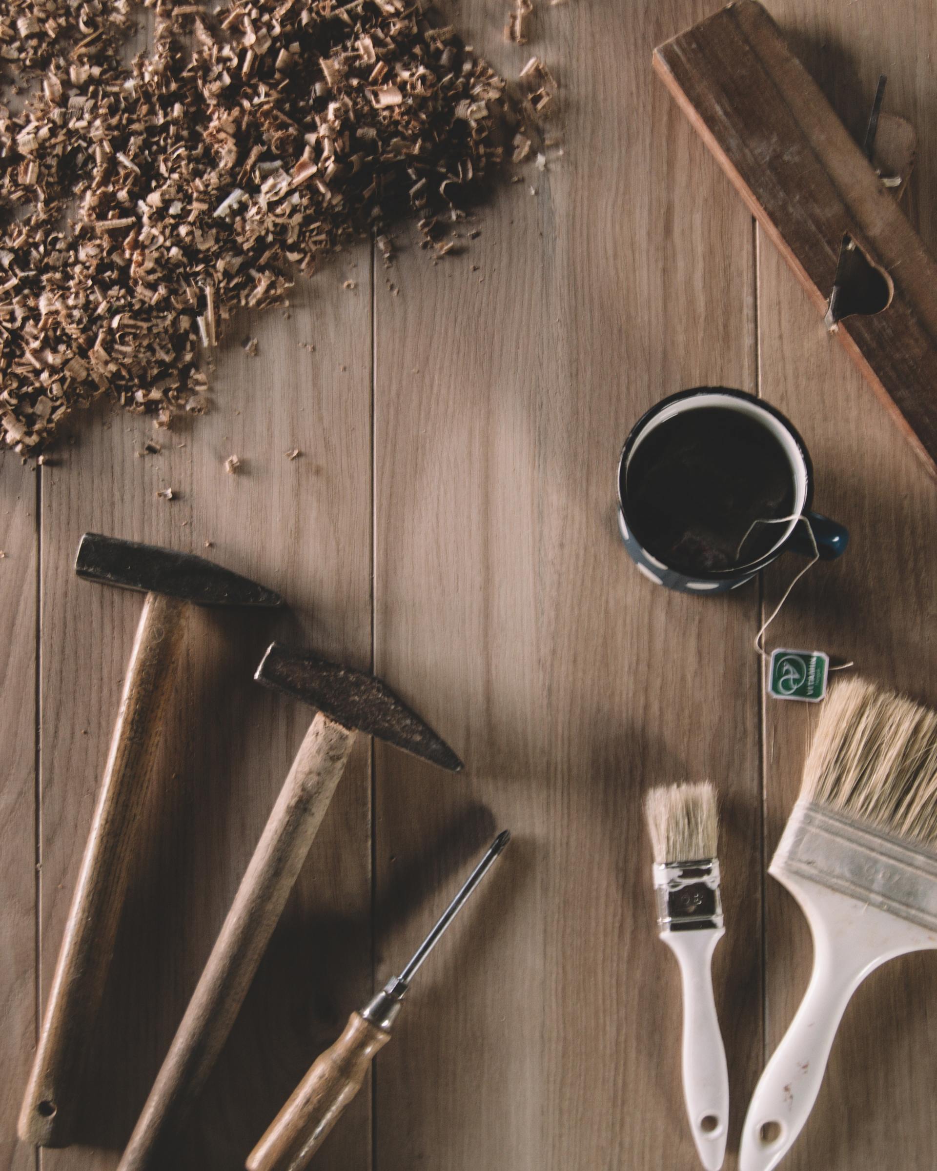 A wooden table topped with a hammer , brushes , and wood chips.