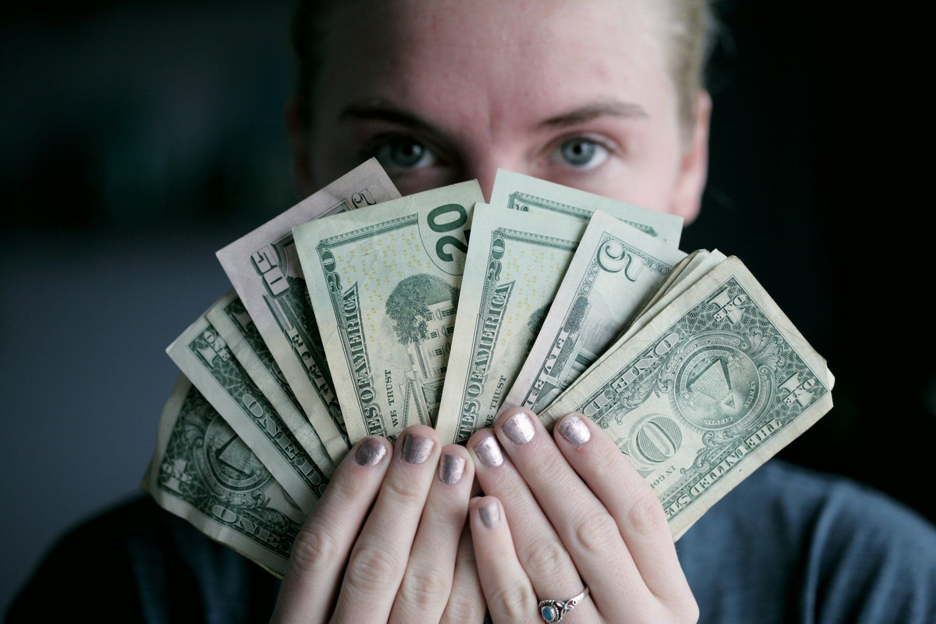 A woman is holding a fan of money in front of her face.