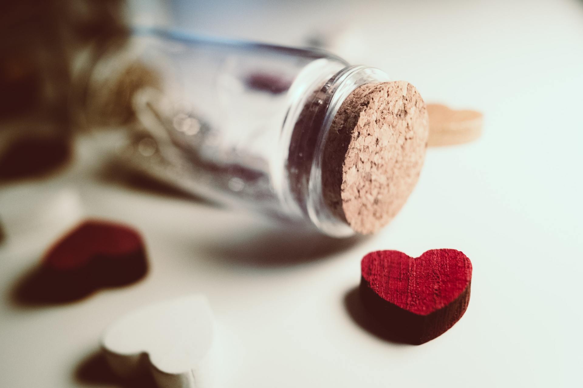 A glass bottle with a cork and a red heart on a table.