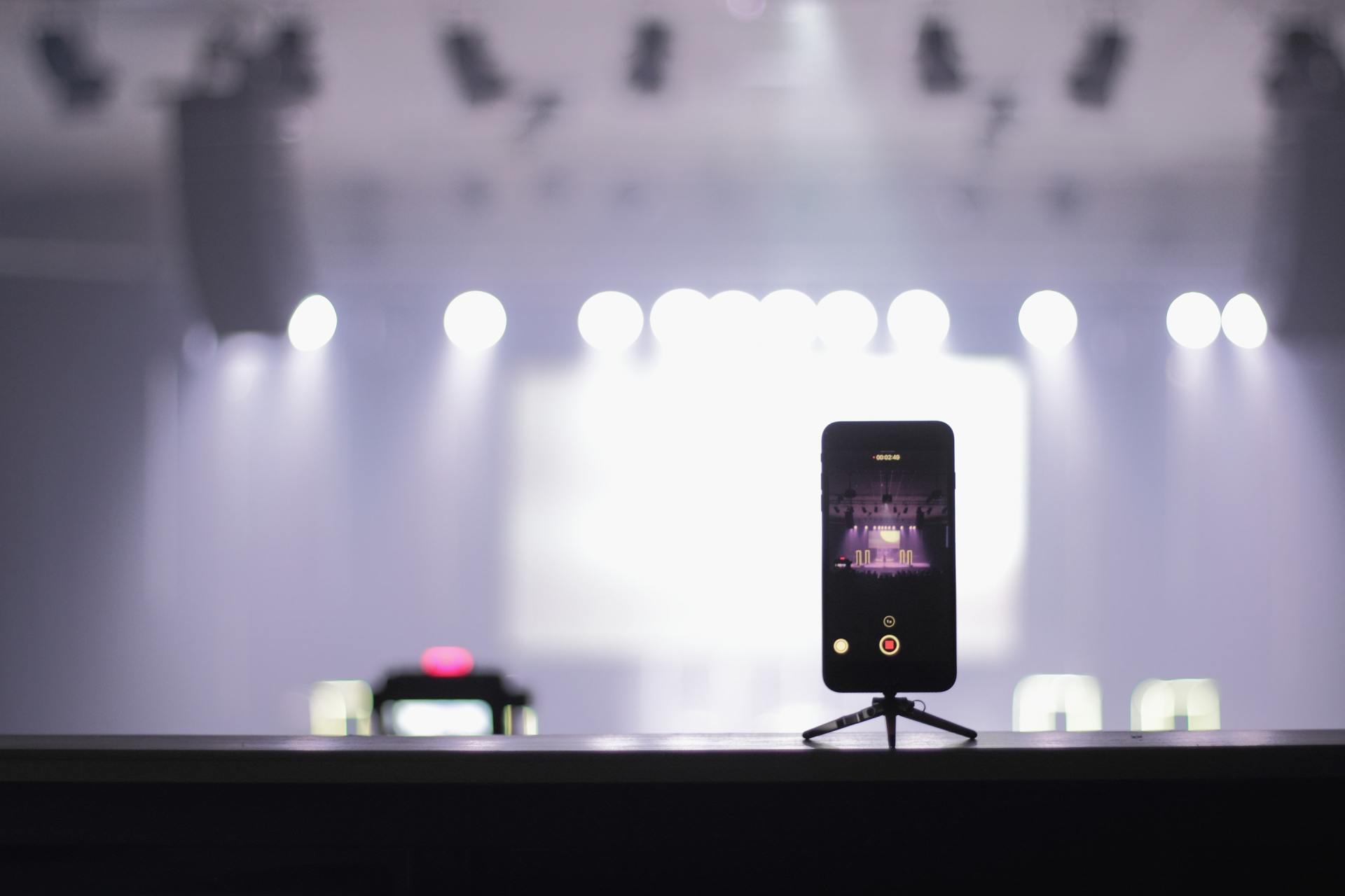 A cell phone is sitting on a tripod in front of a stage.