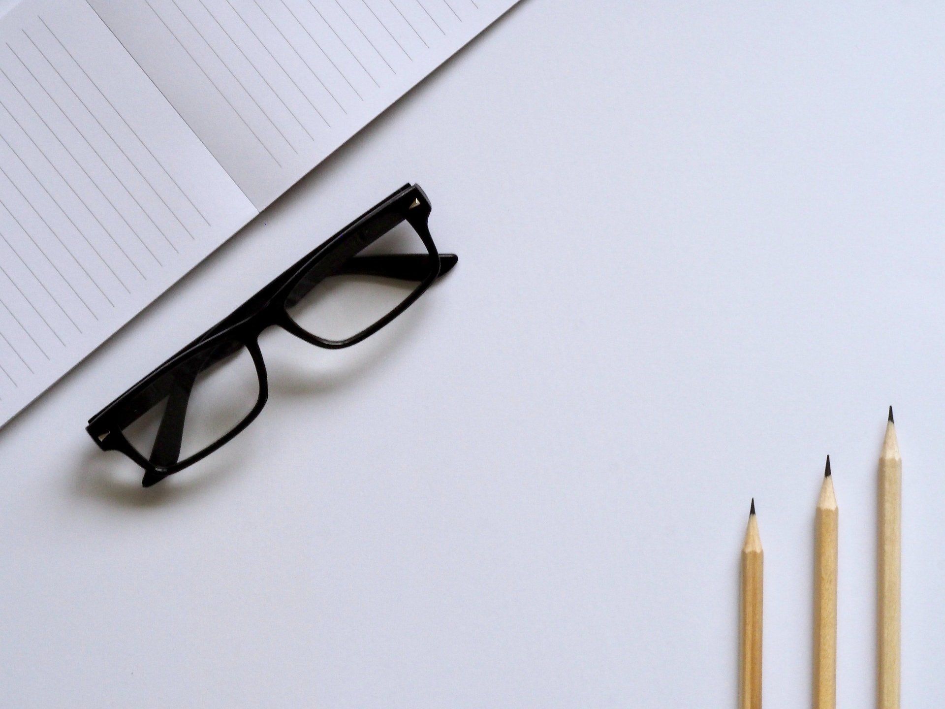 A pair of glasses and three pencils are on a white table.