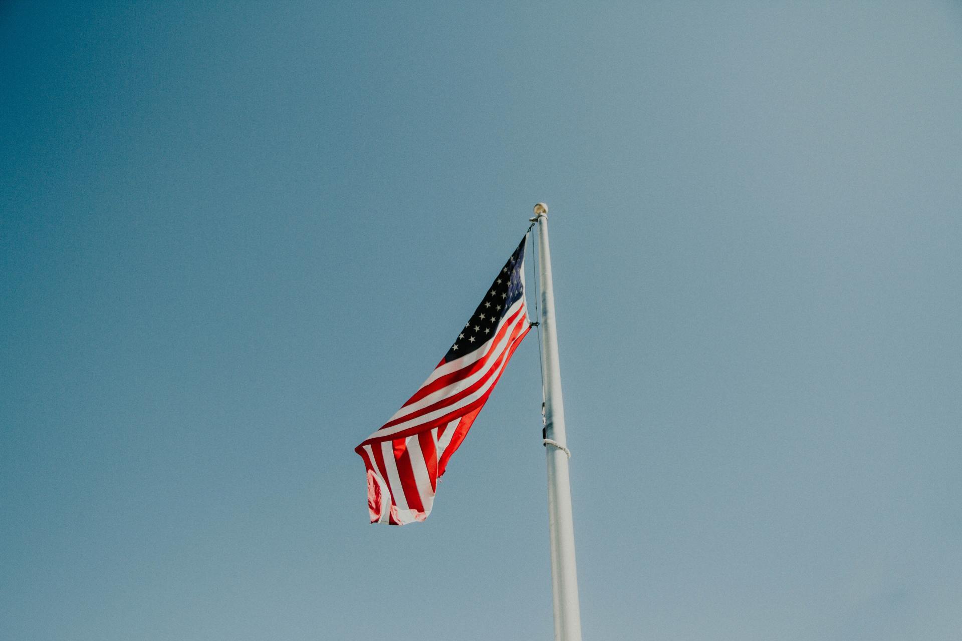 An american flag is flying in the wind on a flag pole.