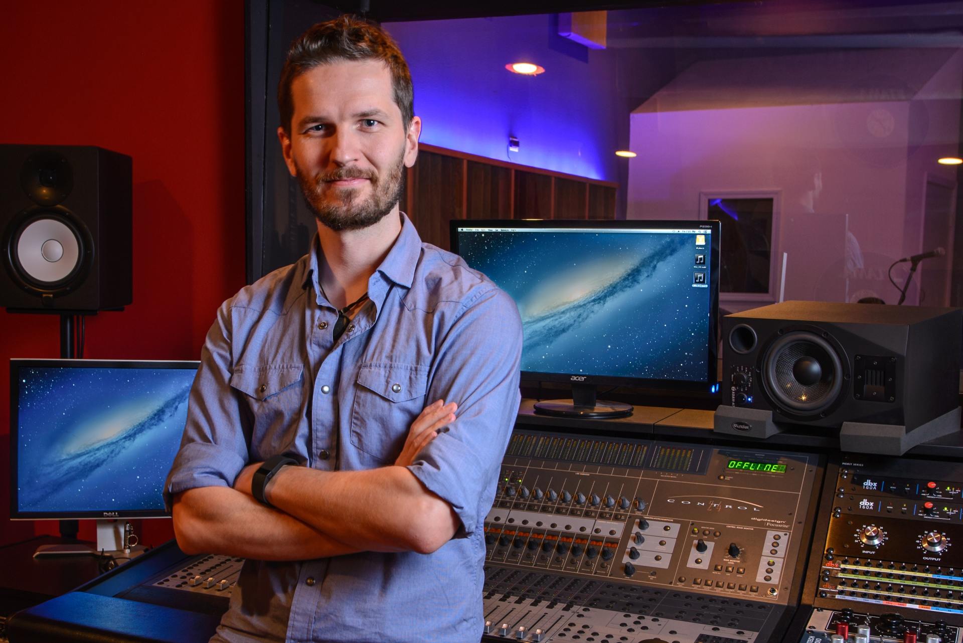A man with his arms crossed stands in front of a sound board