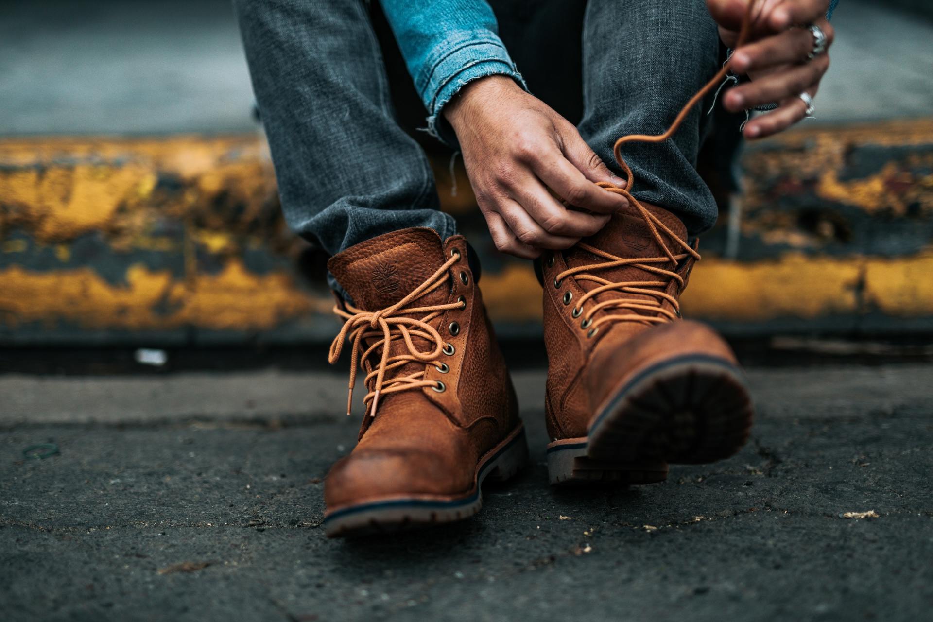 A person is tying their boots on a sidewalk.