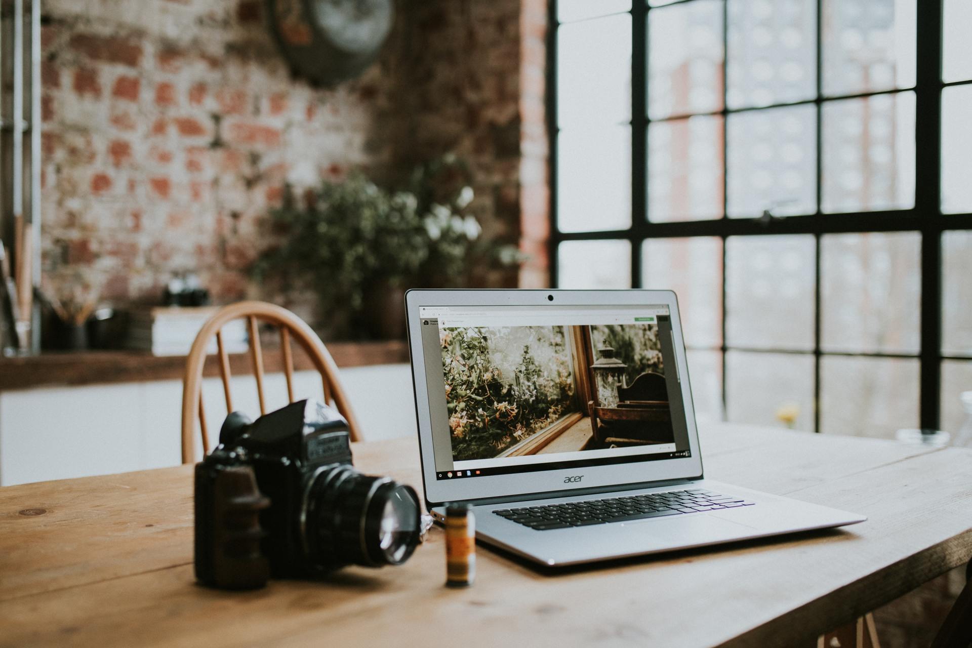 A laptop computer is sitting on a wooden table next to a camera.