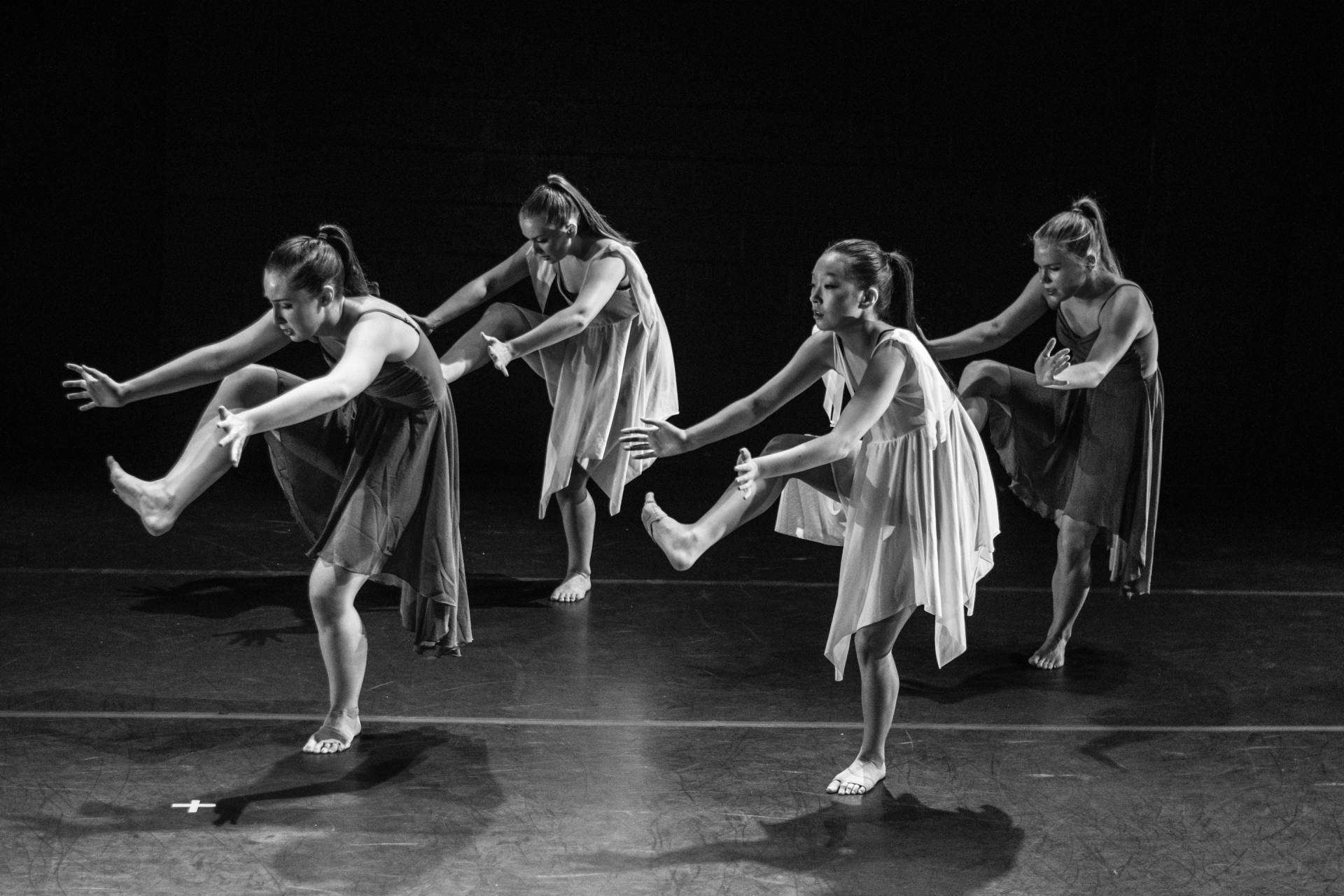 Four women dancers in flowing dresses perform on a stage.