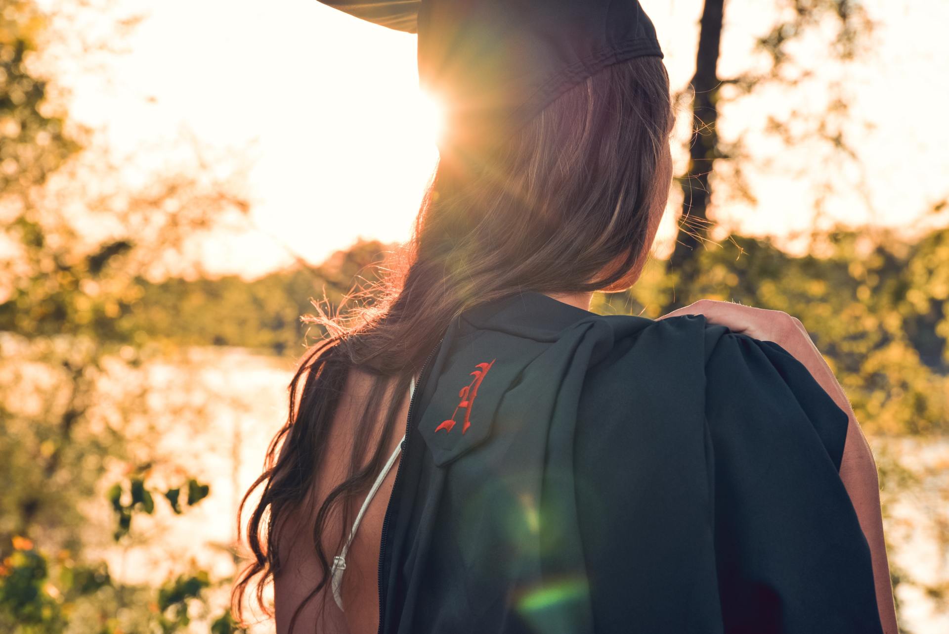 A woman in a graduation cap and gown is standing in front of a lake.