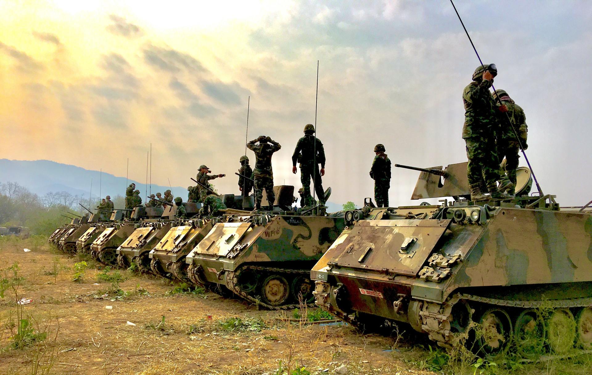 A row of military vehicles are parked in a field.