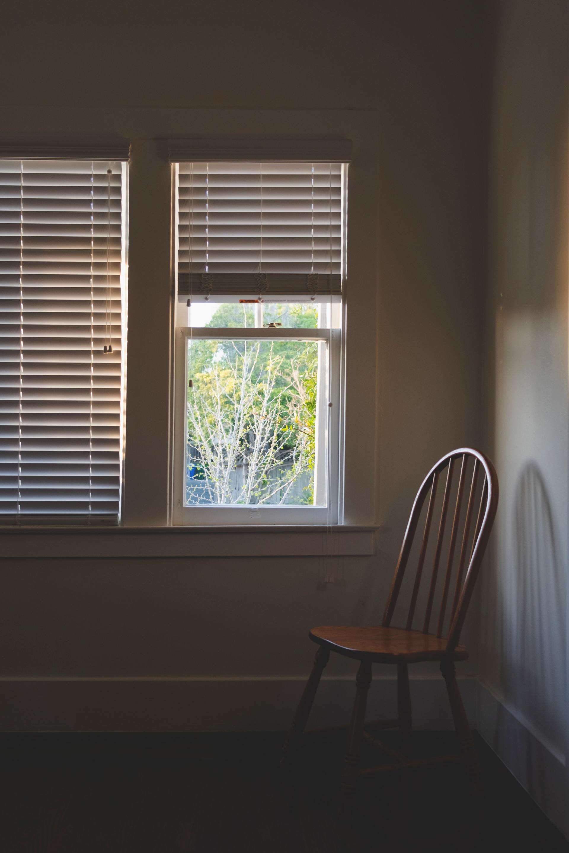A wooden chair is sitting in front of a window with blinds.