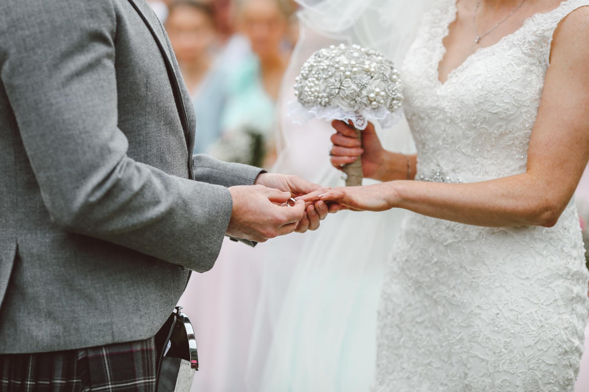 A bride and groom are getting married and the bride is putting the ring on the groom 's finger.