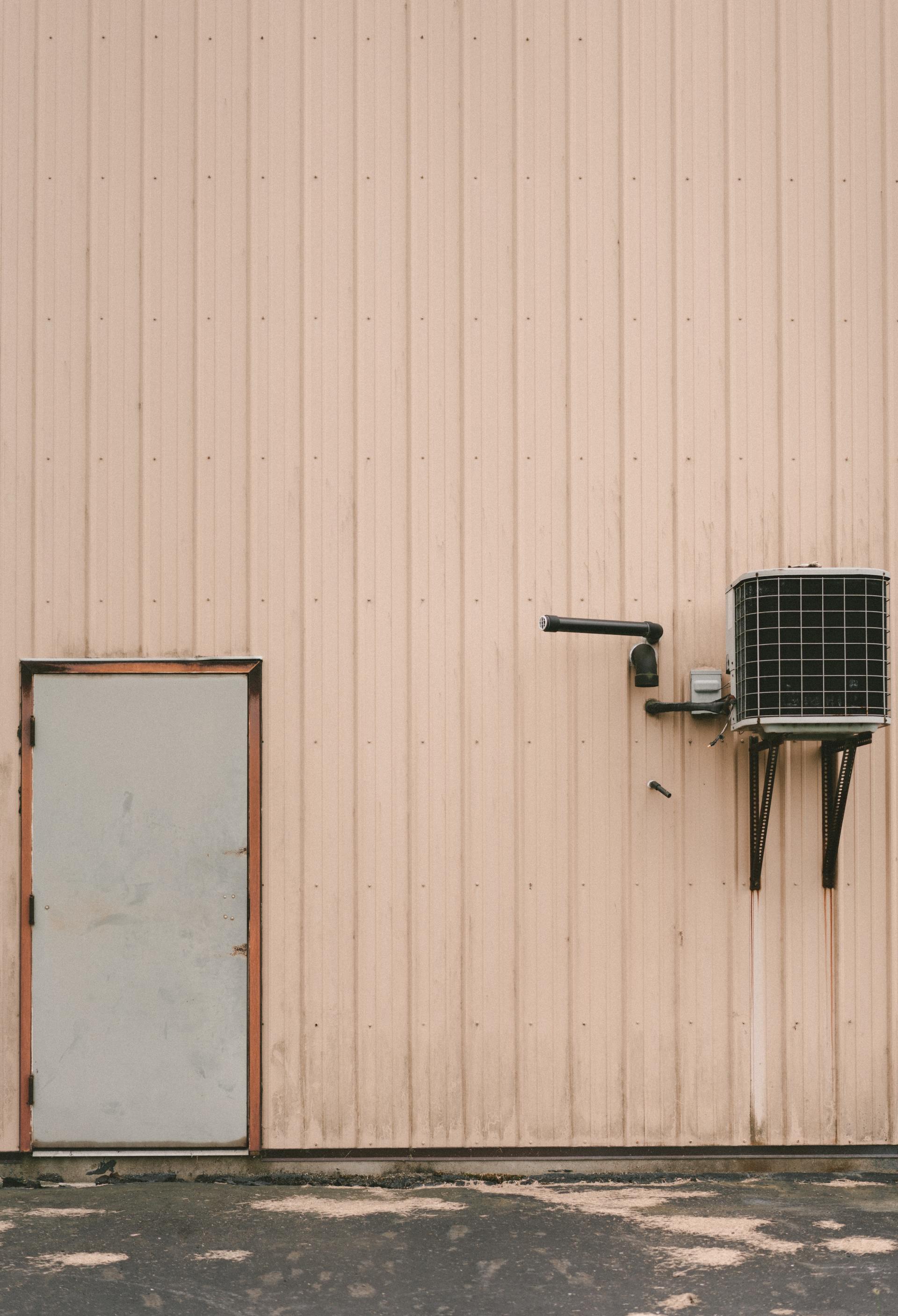 Peach-colored industrial building exterior with a gray door and air conditioning unit.