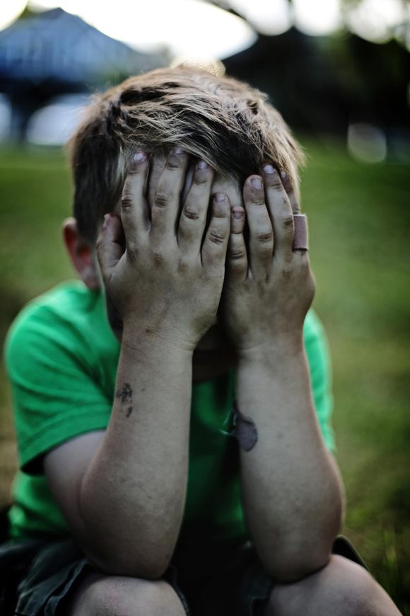 photo of small boy holding head in sadness with dirty hands