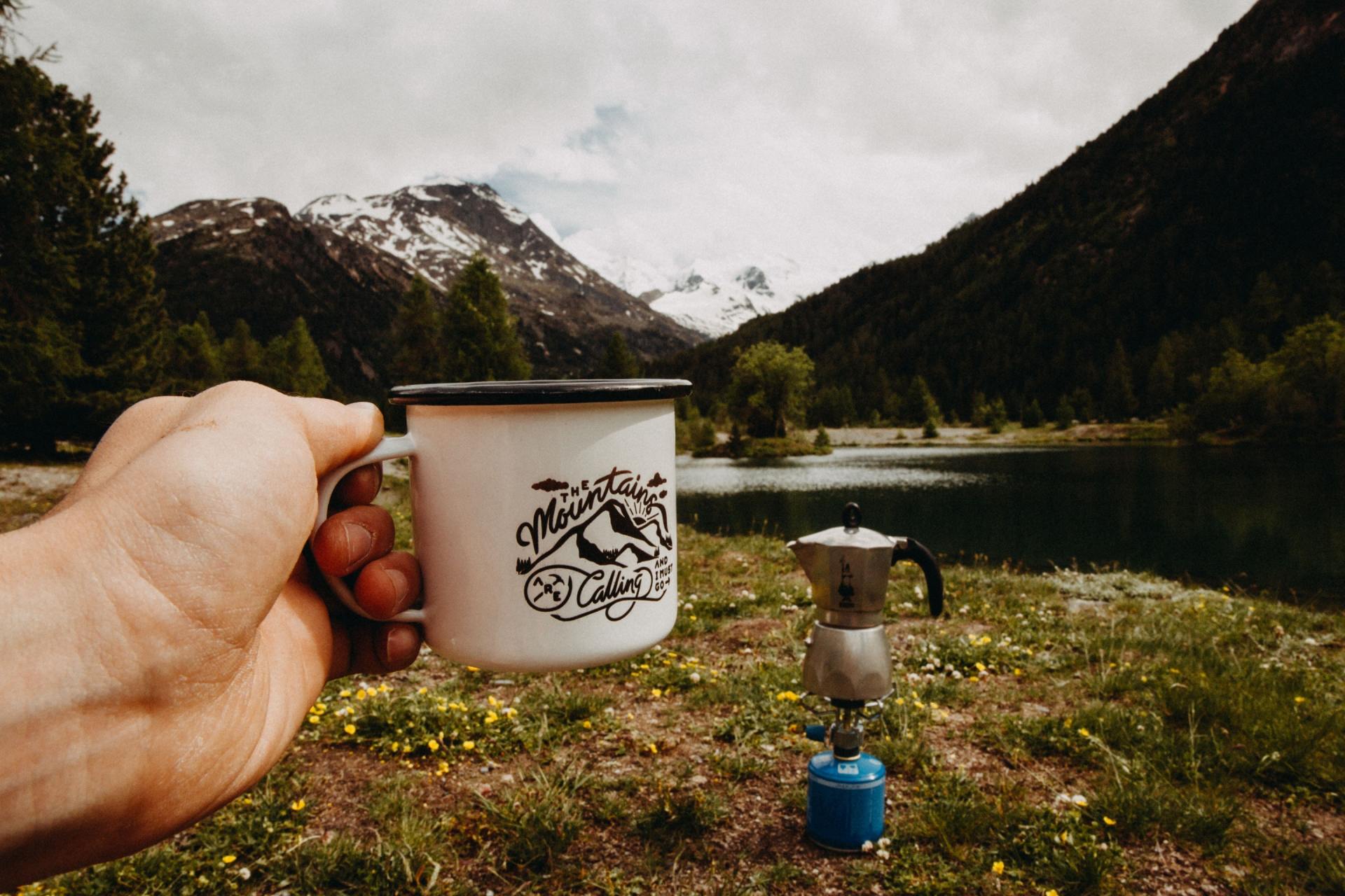 A person is holding a cup of coffee in front of a lake.