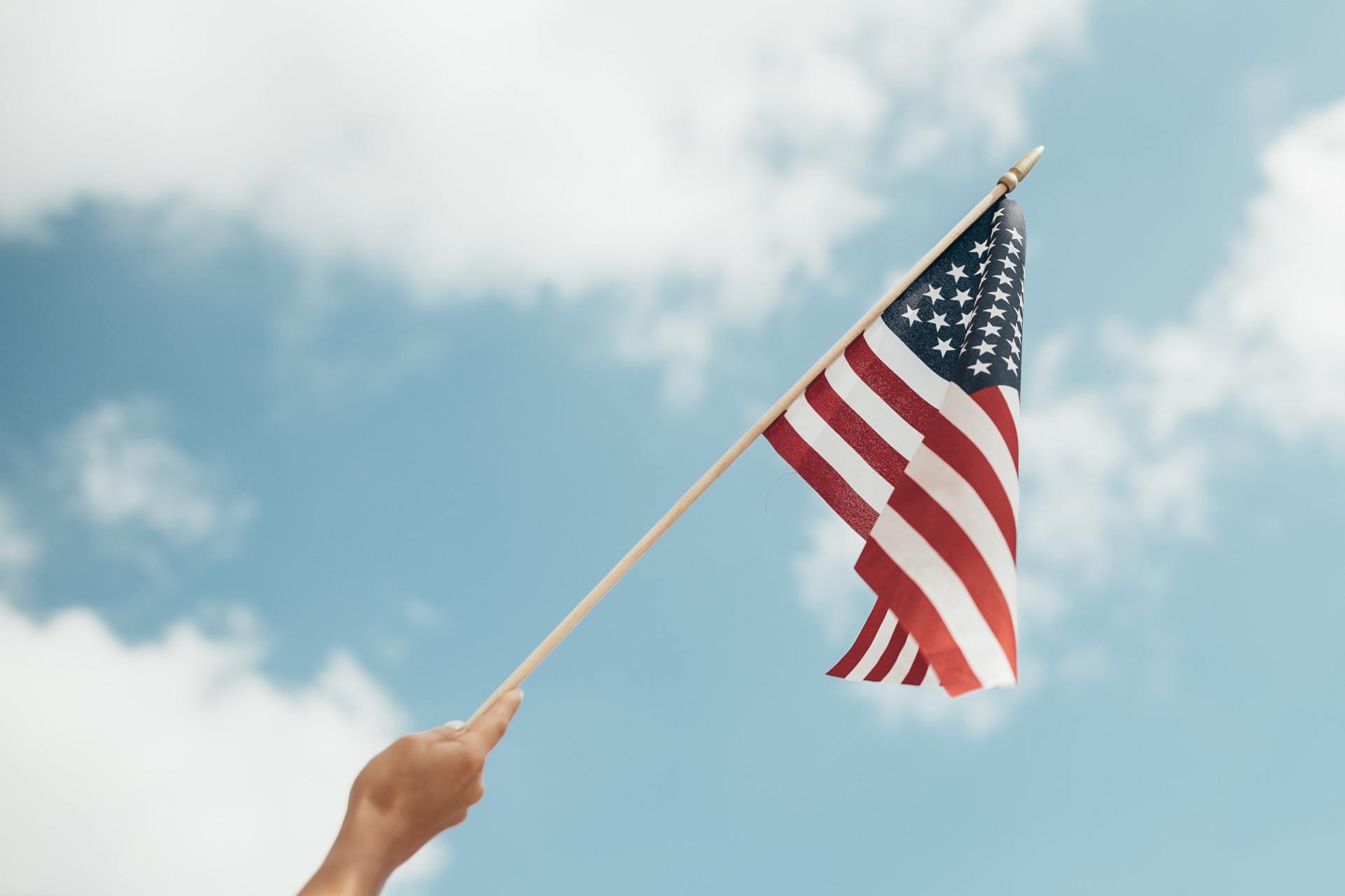 A person is holding an american flag in front of a blue sky