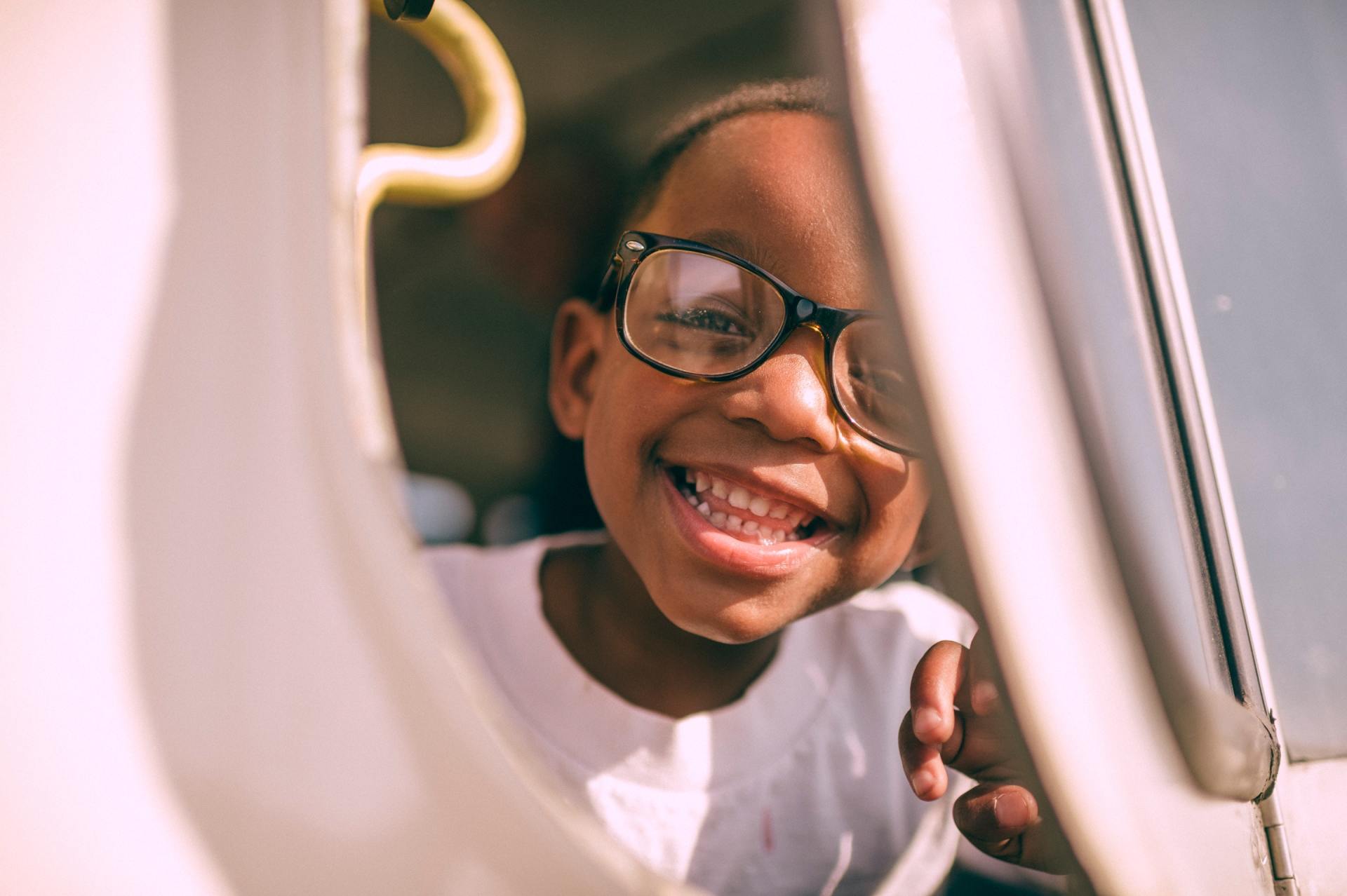 A young girl wearing glasses is smiling while sitting in a car.