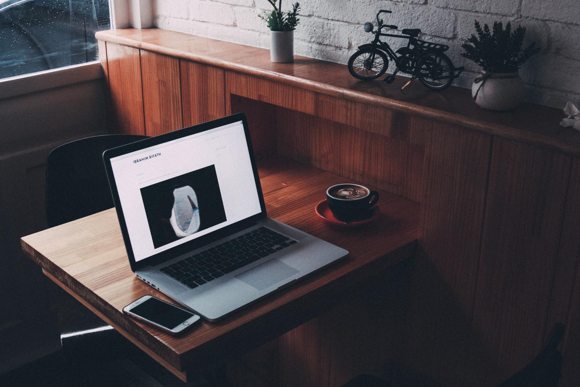 A laptop is sitting on a wooden table next to a cup of coffee and a cell phone.