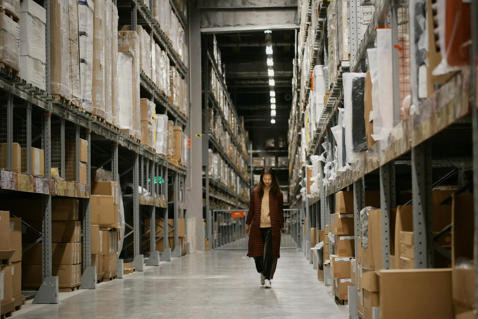 A woman is walking through a warehouse filled with lots of boxes.
