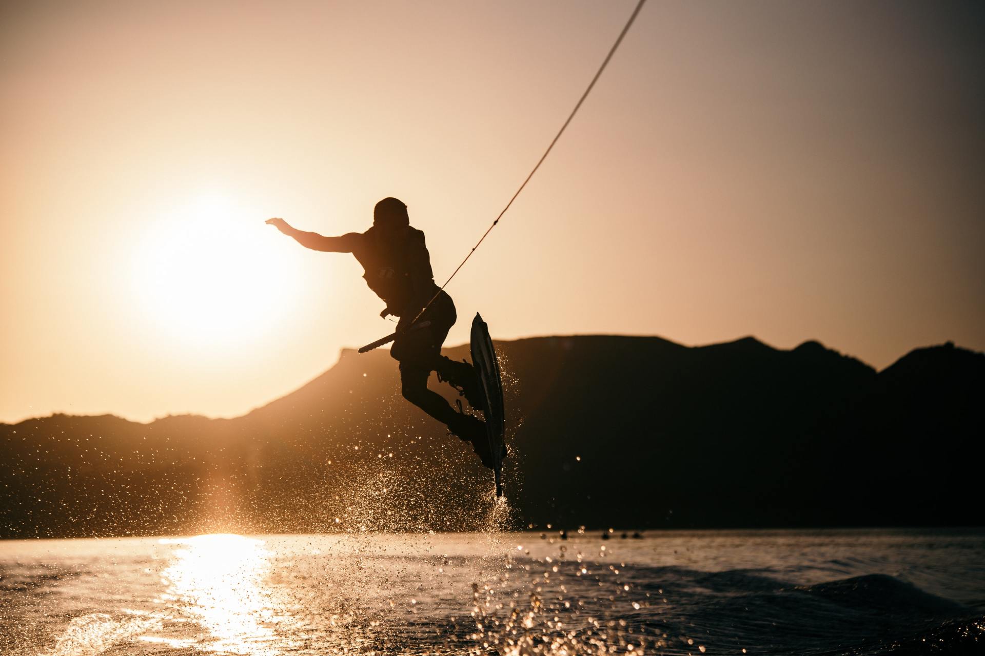 A man is jumping in the air while wakeboarding on a lake at sunset.