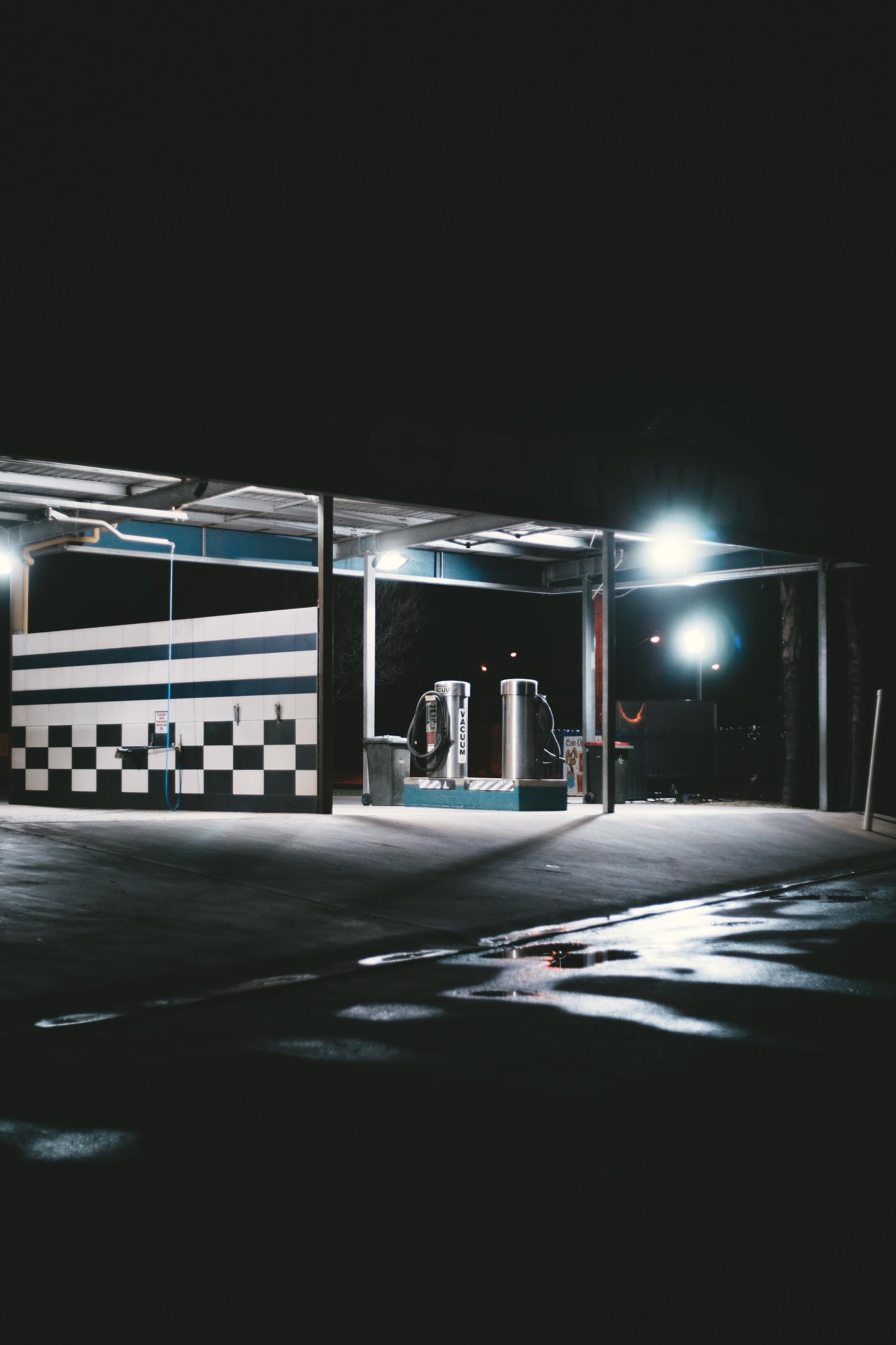 Car wash station lit up at night with checkered wall and vacuum machines.