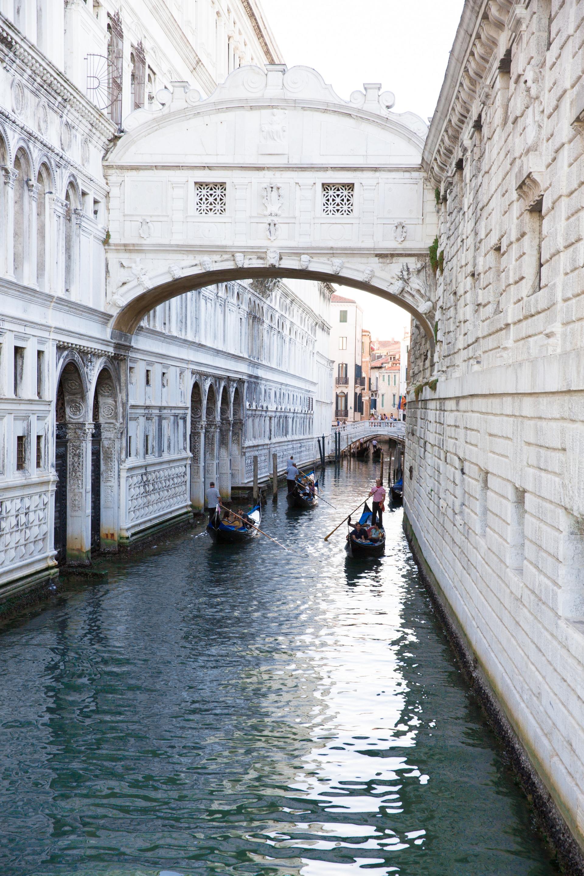 A couple of gondolas are going under a bridge over a canal.