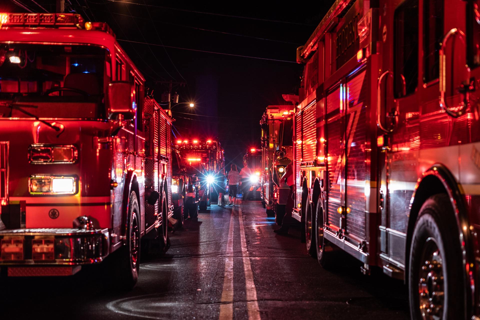 A row of fire trucks are parked on the side of the road at night.