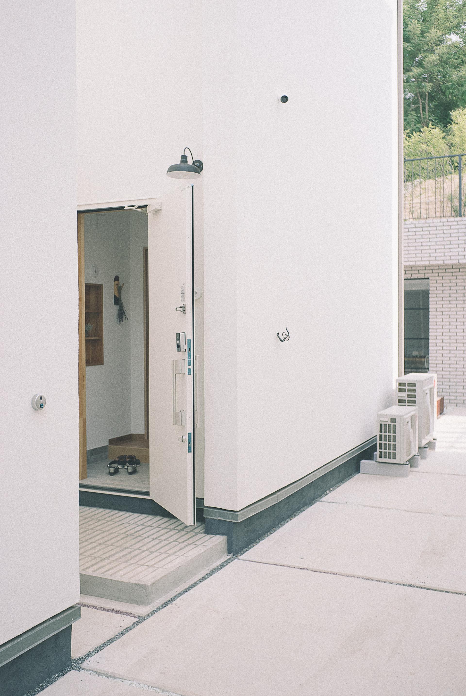 Exterior doorway of a white building with open door, leading to a tiled entryway. Air conditioning units along the wall.