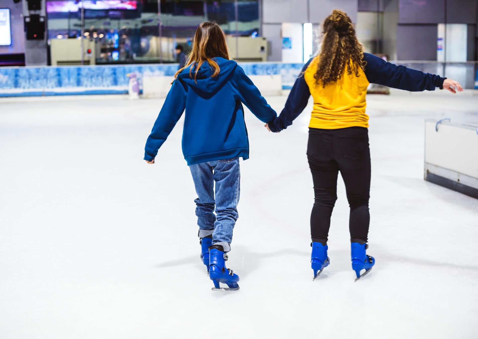 Twee meisjes houden elkaars hand vast terwijl ze schaatsen op een ijsbaan.