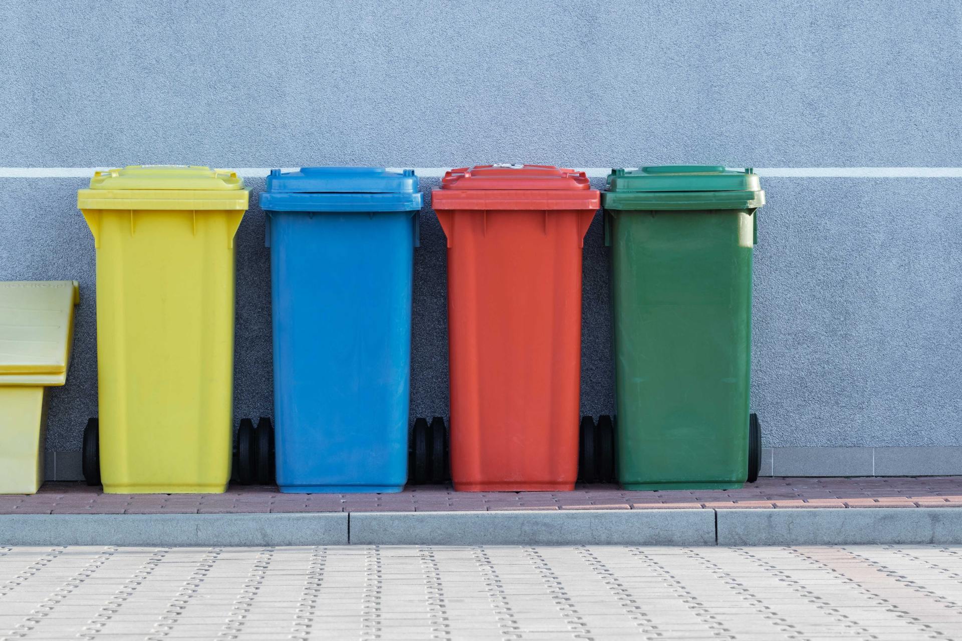 A row of colorful trash cans sitting next to each other on a sidewalk.