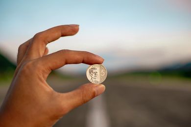 A person is holding a coin in their hand in front of a road.