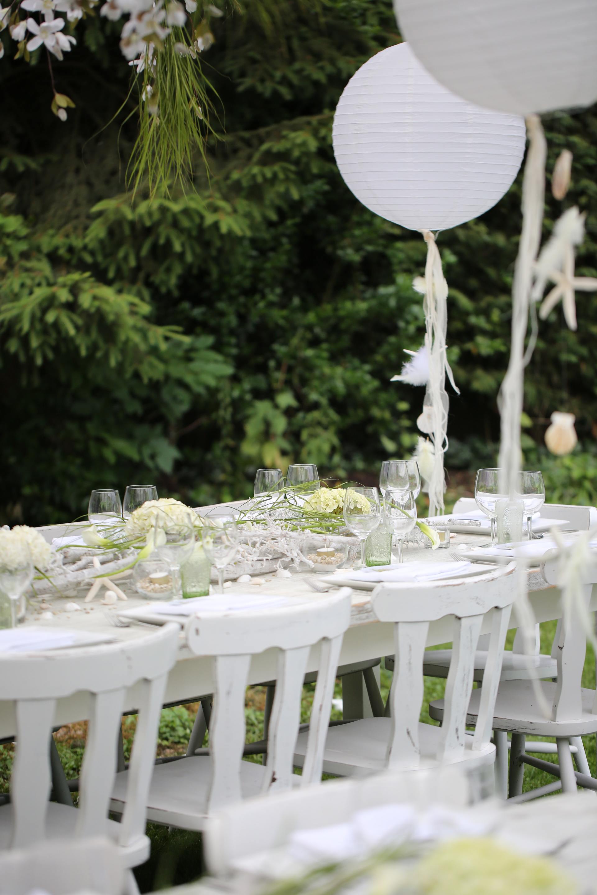Een gedekte tafel voor een huwelijksreceptie met witte stoelen en ballonnen.
