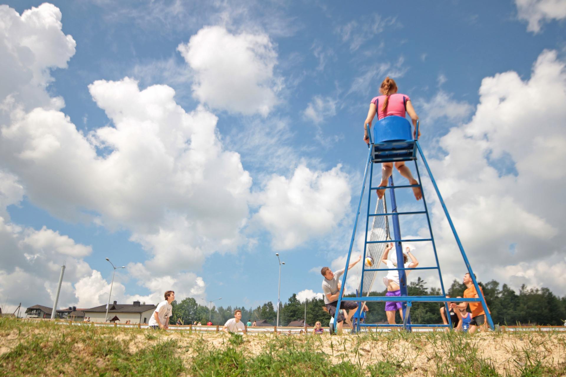 A woman is sitting on a lifeguard chair watching people play tennis.