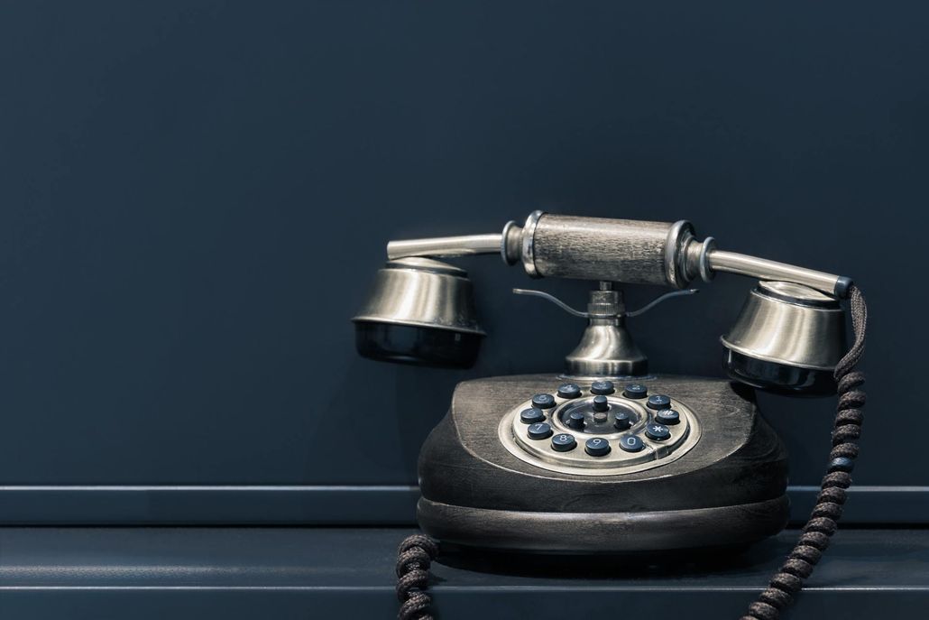 An old black telephone is sitting on a shelf against a blue wall.
