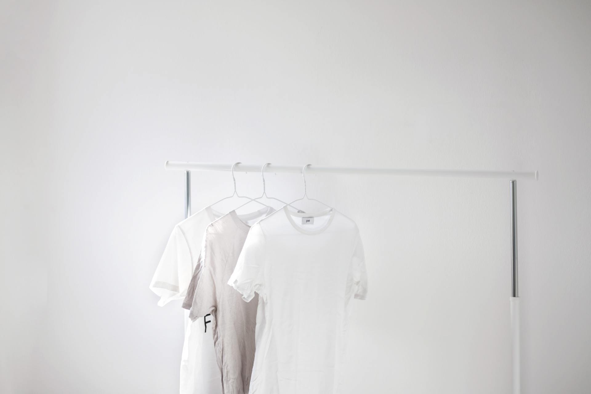 Three white t-shirts are hanging on a rack in a room.