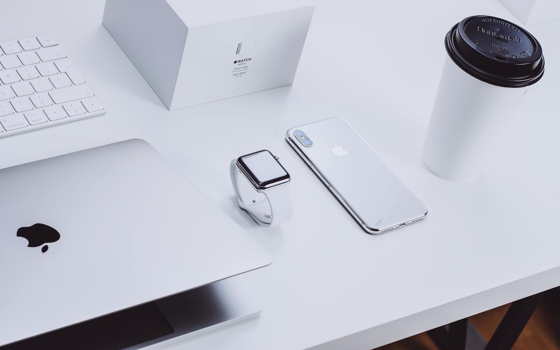 A white desk with a laptop a watch a phone and a cup of coffee