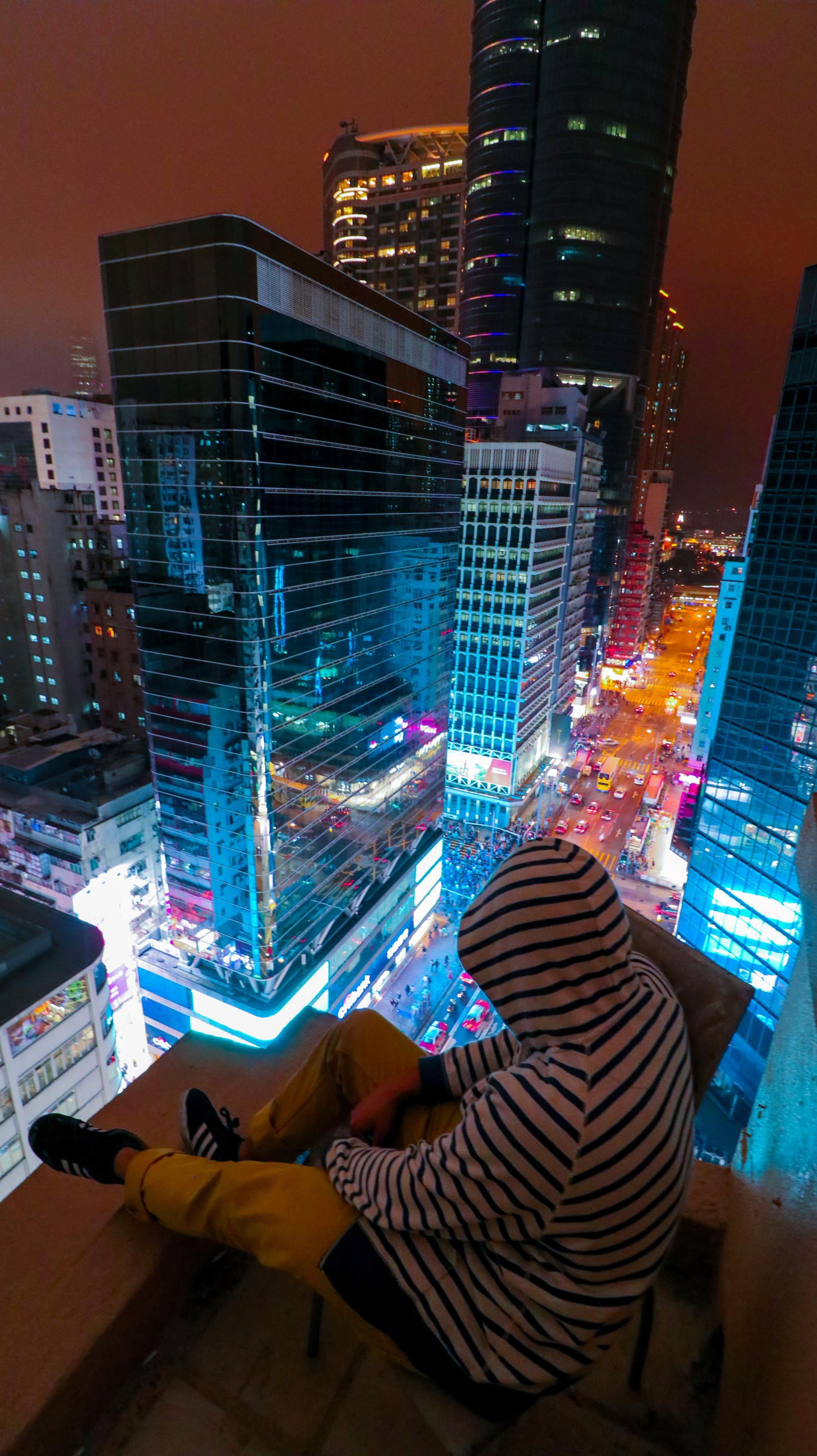 A person is sitting on a balcony overlooking a city at night.