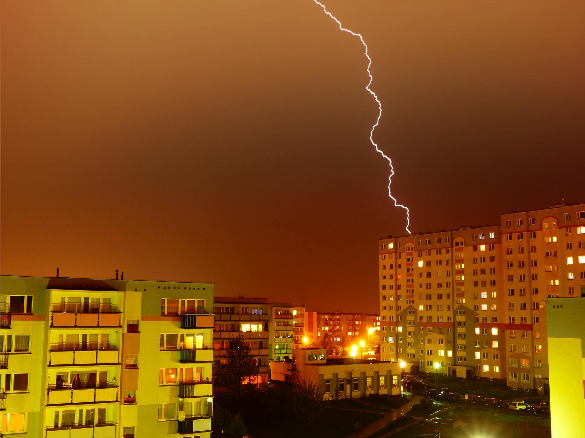 La foudre frappe un grand bâtiment la nuit dans une ville, avec d'autres bâtiments illuminés à proximité.
