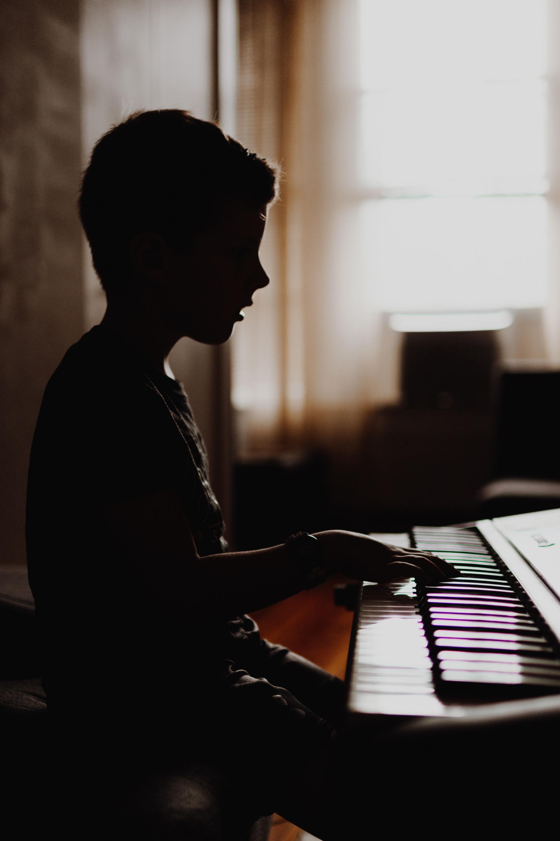 A young boy is playing a piano in a dark room.