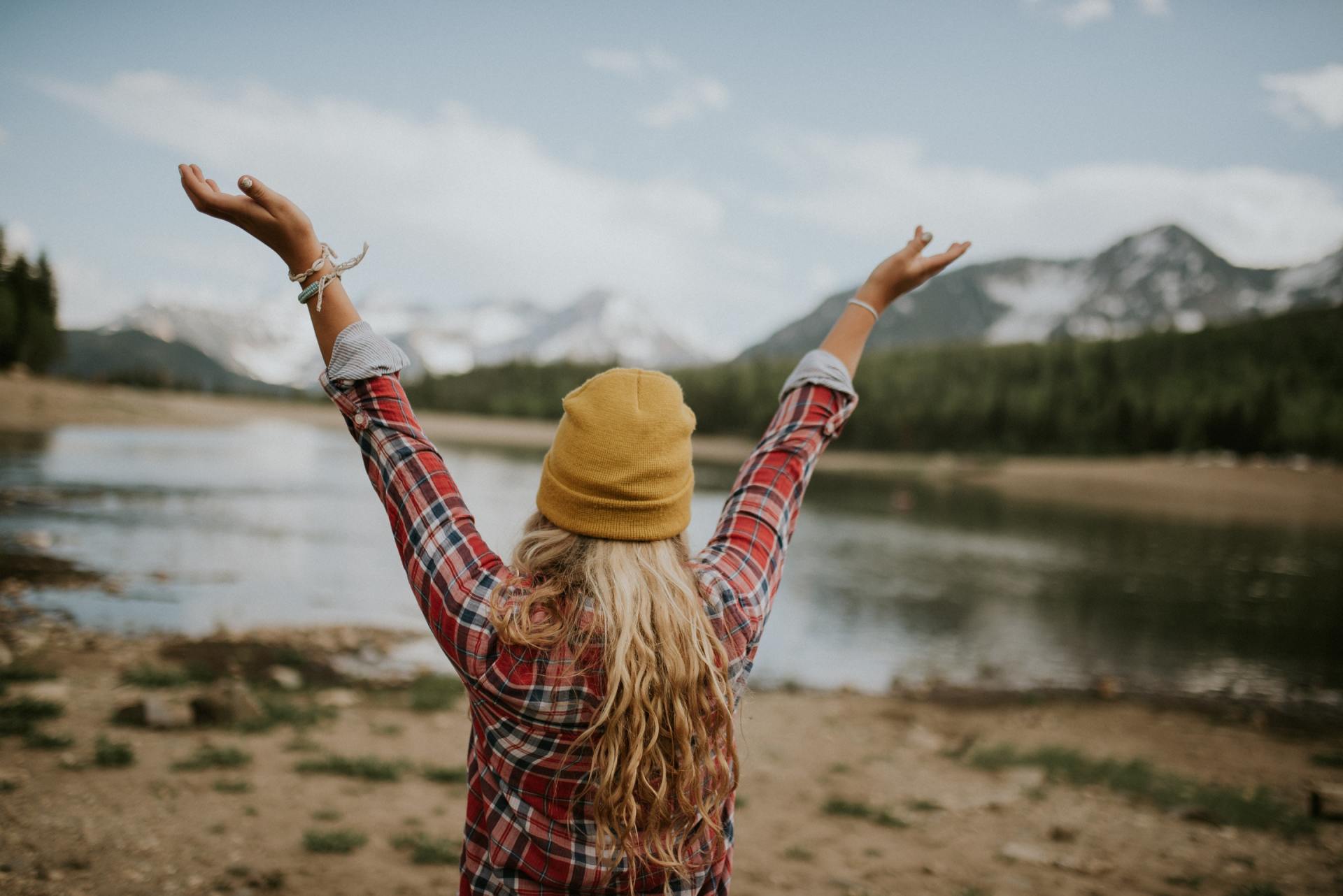 Blonde hair girl at a mountain lake with her arms up in the air