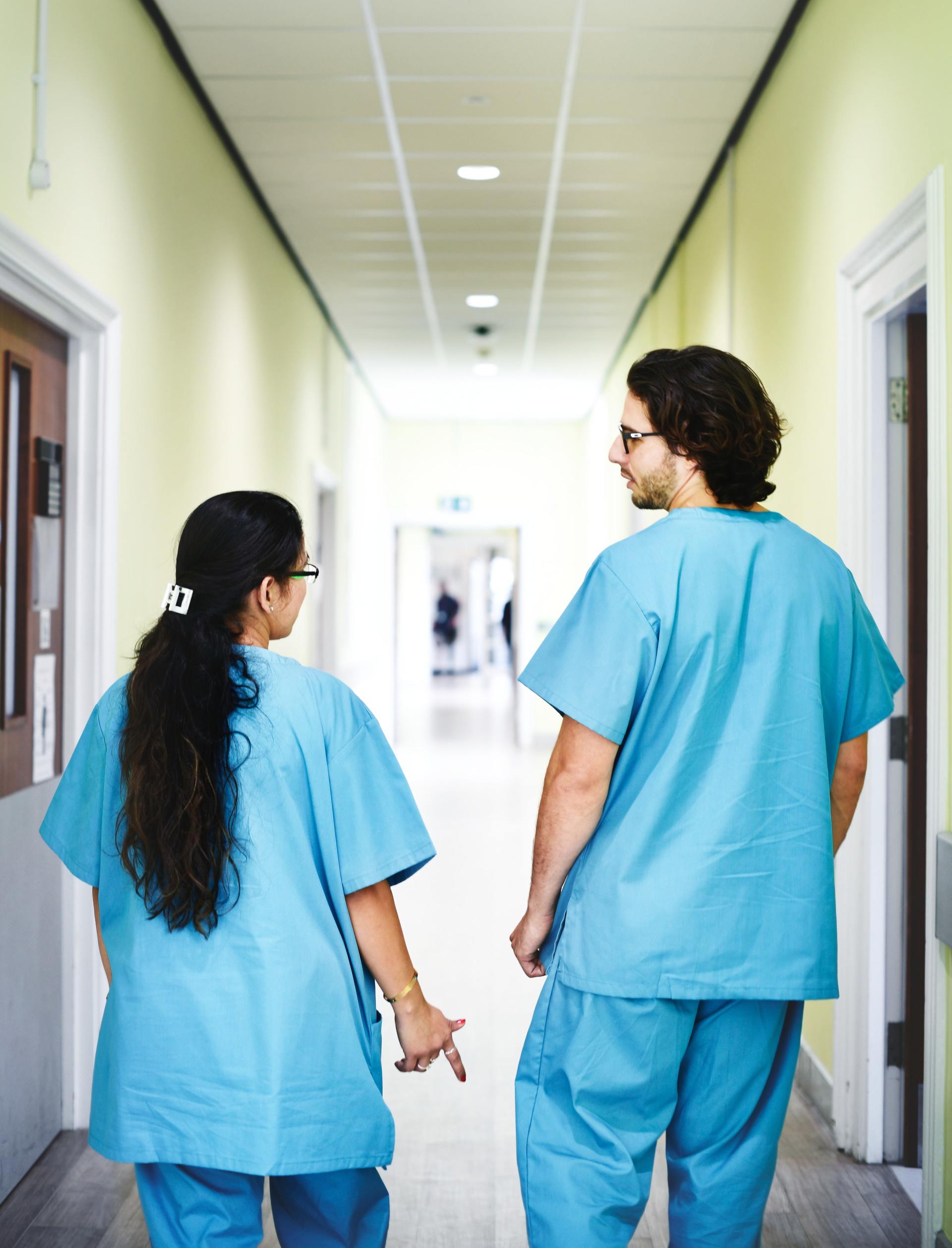 A man and a woman in scrubs are walking down a hospital hallway