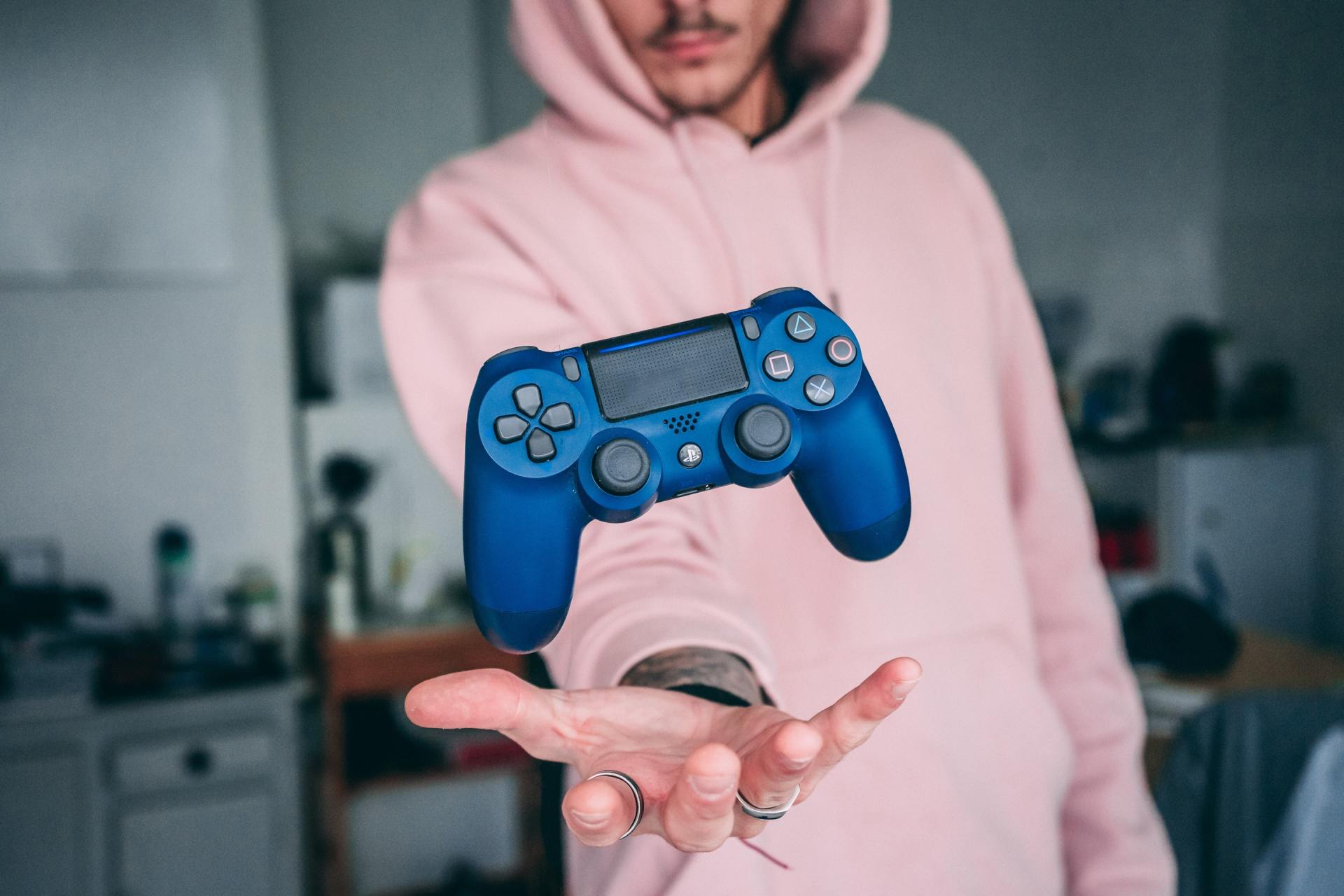 man in a pink hoody with his open palm out, a ps4 controller overs over his hands