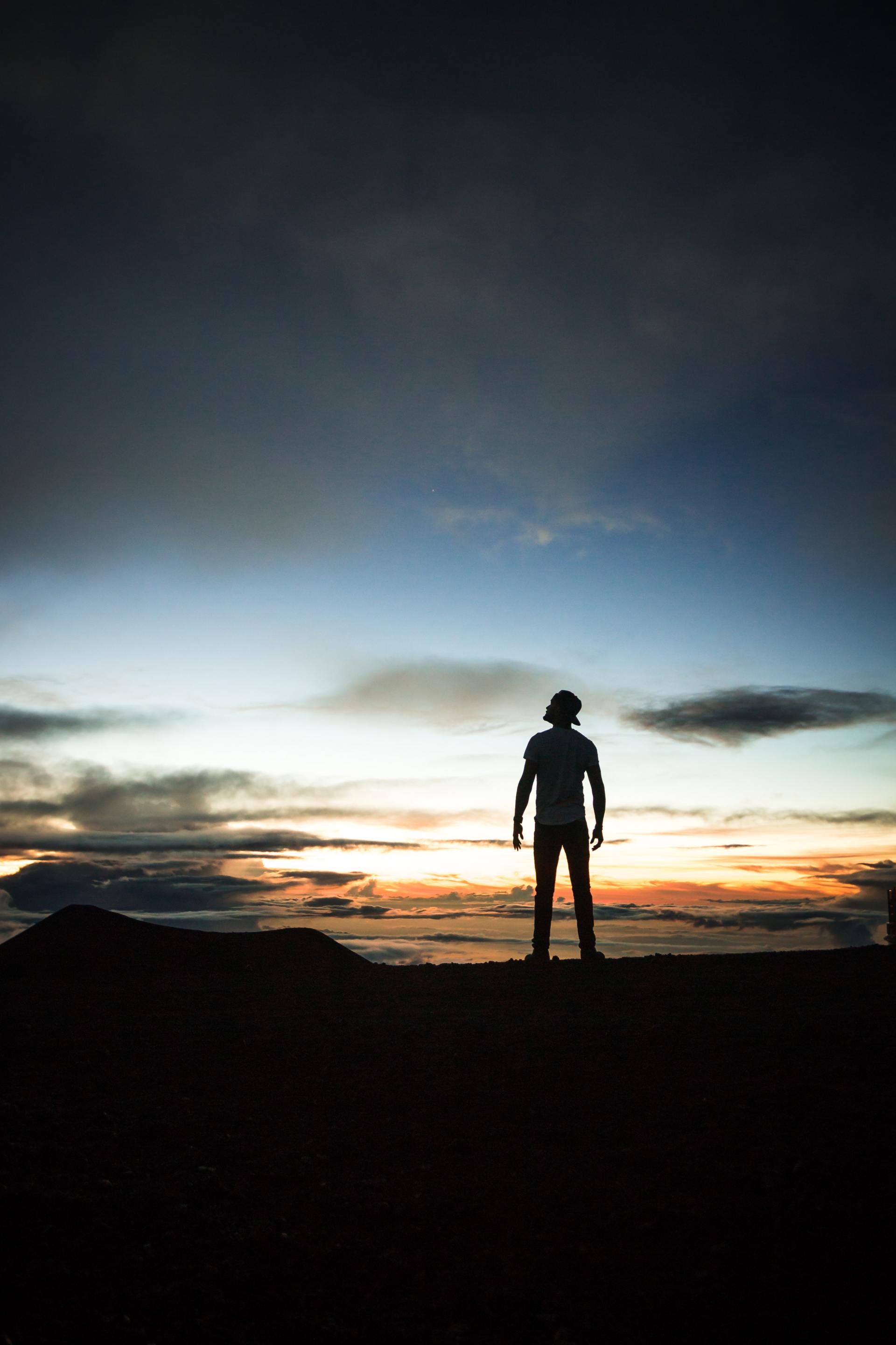 A silhouette of a person standing on top of a hill at sunset.